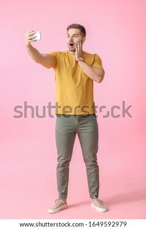 Shocked young man taking selfie on color background