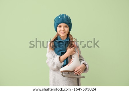 Cute little girl with ice skates on color background