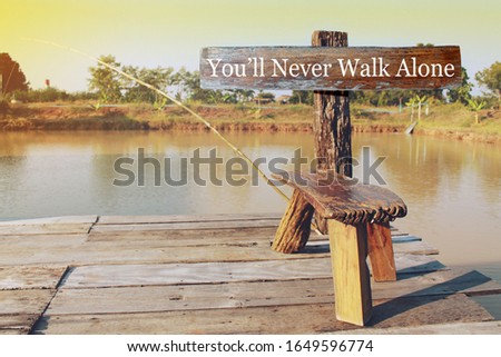 Wooden sign written You'll never walk alone on the waterfront wooden balcony background