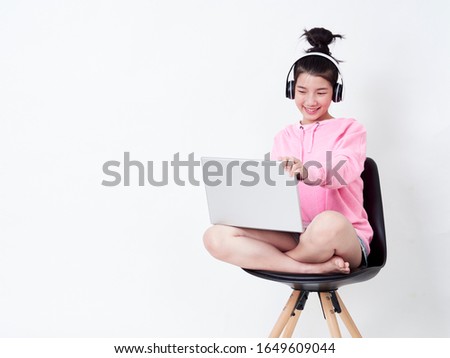 Portrait of cute girl using laptop with headphone while sitting on chair on white background.