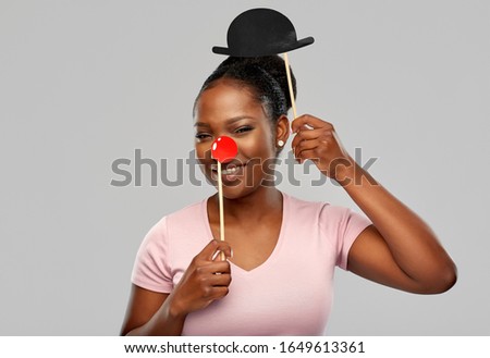 red nose day, party props and photo booth concept concept - happy african american young woman with clown nose over grey background