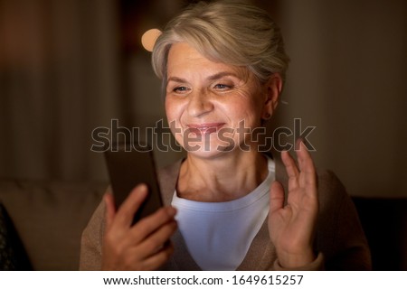 technology, old age and people concept - happy senior woman with smartphone having video call and waving hand at home in evening Royalty-Free Stock Photo #1649615257