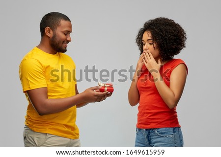 holiday, greeting and people concept - happy african american couple with small red gift box over grey background