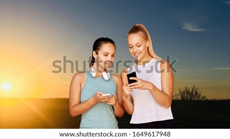 fitness, sport and healthy lifestyle concept - smiling young women or female friends with smartphones over sunset sky on background