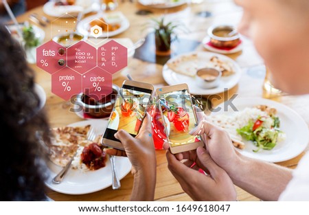 technology, eating and people concept - hands of couple with cocktail drinks in mason jar glasses on smartphone screens and nutritional value chart at restaurant