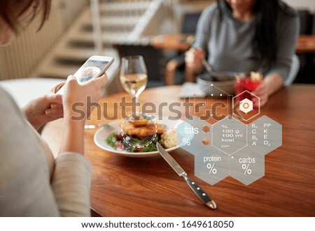 new nordic cuisine, technology and people concept - woman with food on smartphone screen and nutritional value chart r at restaurant