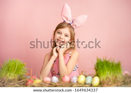 Cute little baby wears bunny ears on Easter day. Cute little girl with easter eggs and green grass. blue background