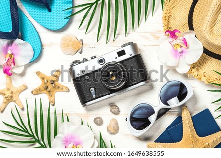Summer travel background. Old film camera, hat, flip flops, shell and palm leaves on white background.
