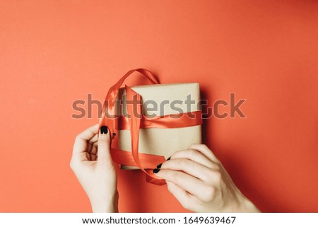 Partial view of woman tying ribbon on gift box isolated on red