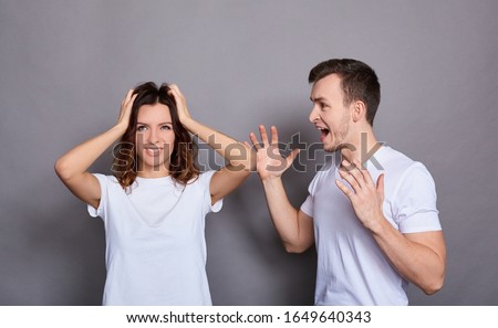Couple of young woman and man in white basic t-shirts and feuds standing isolated over gray background. The concept of a crisis of relations, family problems, domestic violence. Royalty-Free Stock Photo #1649640343