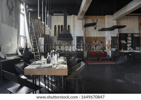 dark design of huge studio apartment in loft style with big windows and black wooden contemporary furniture with free planing. view of large dining table server with white plates, glasses and candles.