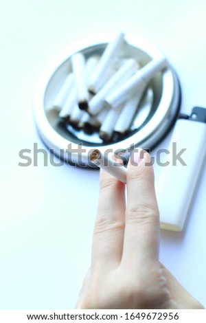 a cigarette butt in a female hand on a background of a full ashtray and a lighter