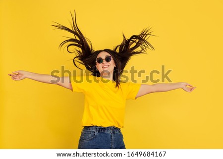 Inspired dancing in sunglasses. Caucasian woman on yellow studio background. Beautiful female brunette model in casual style. Concept of human emotions, facial expression, sales, ad, copyspace.