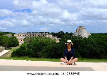 An Asian female tourist is posing for a picture with view of the ruins in Uxmal, an ancient Maya city of the classical period located in present-day Mexico.