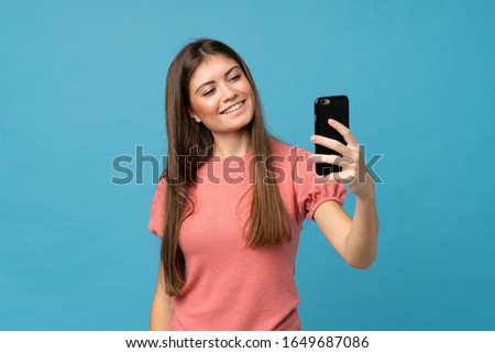 Young woman over isolated blue background taking a selfie with the mobile