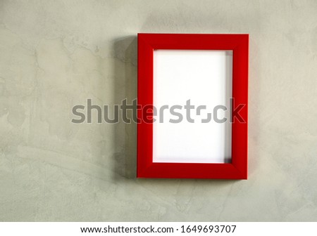 Red square picture frame hung on a gray cement wall.