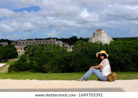 An Asian female tourist is posing for a picture with view of the ruins in Uxmal, an ancient Maya city of the classical period located in present-day Mexico.