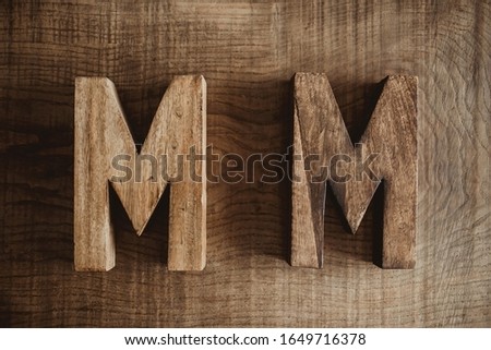 Two M letters made of wood. Name and surname, family name initials. Carpentry business background.
