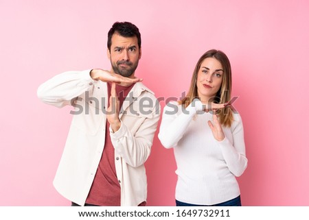 Couple in Valentine Day over isolated pink background making stop gesture with her hand to stop an act
