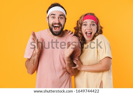 Portrait of athletic young cheerful couple wearing headbands screaming together in surprise isolated over yellow background