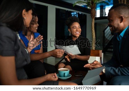 Laughing group of a young African businesspeople going over paperwork together during a casual meeting over coffee in an office