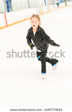 Little figure skater practicing on an indoor ice arena.