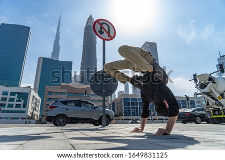 Flexible Acrobat keep balance on the hands with blurred Dubai cityscape and traffic sign U-Turn is prohibited. Concept of modern, business and unlimited possibility 