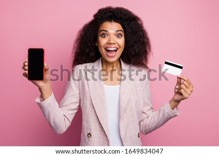 Photo of beautiful excited dark skin lady hold plastic credit card showing new model telephone advising online payment wear checkered plaid blazer isolated pink pastel color background