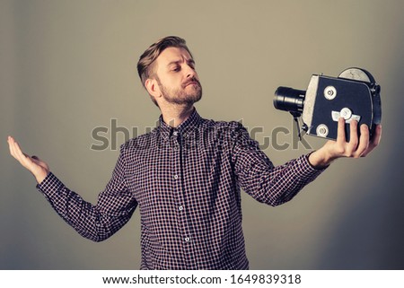 Young attractive cameraman in a plaid shirt takes himself off to an old movie camera. Selffi concept