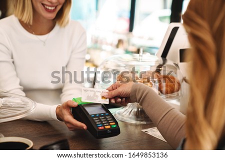 Cropped photo of mature woman paying credit card in cafe while waiter holding payment terminal