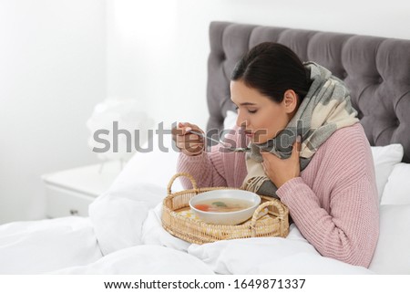 Sick young woman eating soup to cure flu in bed at home. Space for text