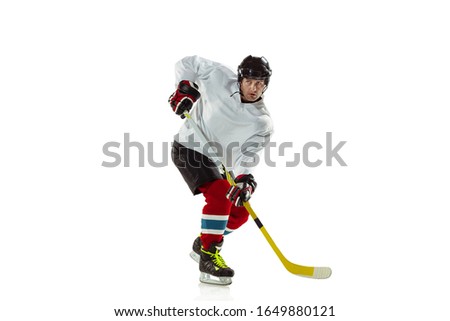 Scoring. Young male hockey player with the stick on ice court and white background. Sportsman wearing equipment and helmet practicing. Concept of sport, healthy lifestyle, motion, movement, action.