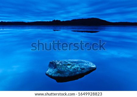 Rock on blue waters of lake Rådasjön, Sweden, Europe