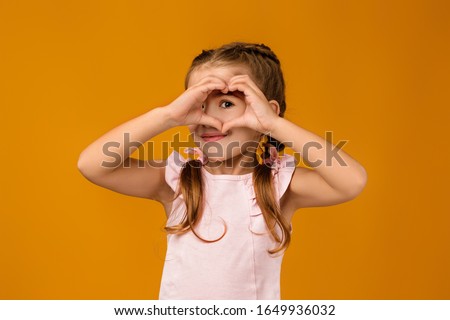Cute smiling little child girl making heart-shape gesture on blue background.