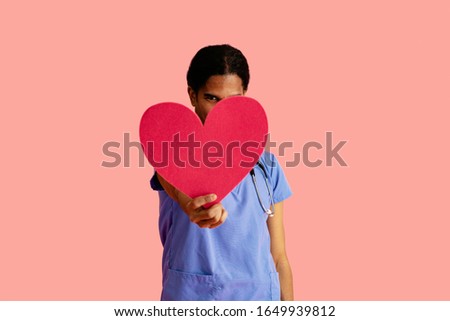 Studio portrait of a male doctor or nurse wearing blue scrubs holding heart cutout