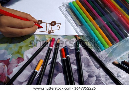 A child draws on the table with multi-colored felt-tip pens and pencils in an album