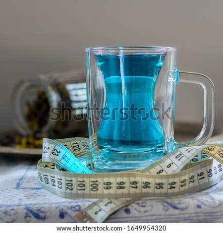 Butterfly pea flower blue tea in glass mug with silhouette like slim woman figure. With measuring tape around as drink helps to loose weight. Healthy thai detox herbal beverage. Square