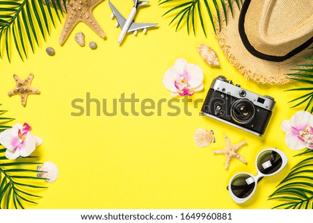 Summer travel flat lay background. Old film camera, hat, shell and palm leaves on yellow background.