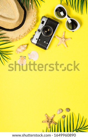 Summer travel concept. Old film camera, hat, shell and palm leaves on yellow background.
