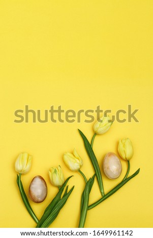 Easter pattern from blooming yellow flowers tulip and easter eggs with stone texture with copy space. Spring flowers for holiday. Flat lay, vertical format.