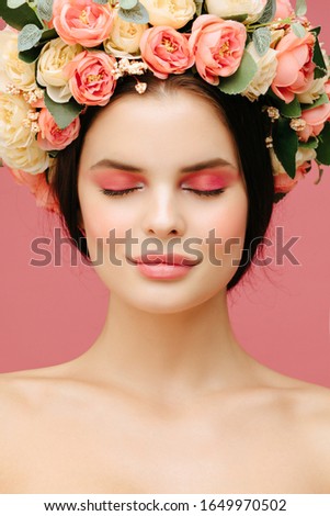 Spring portrait. Young beautiful woman in peonies flowers wreath posing agaist pink background