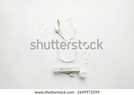 Figure eight of white ribbon with beautiful white eustomas on a white background with colored confetti of hearts, flat lay. 8 March, International Women's Day.