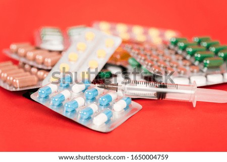 selective focus of syringe near pills in blister packs on red
