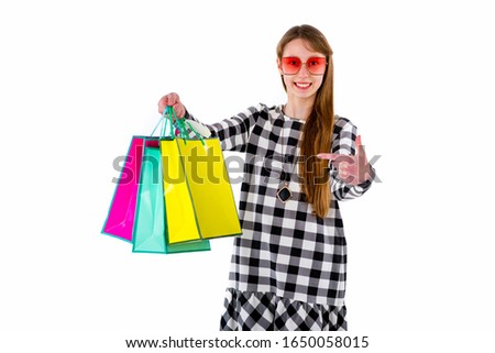 Gesturing handsome european girl smiling and shows to shopping colored bags,isolated white studio background.Mock up,copy space.
