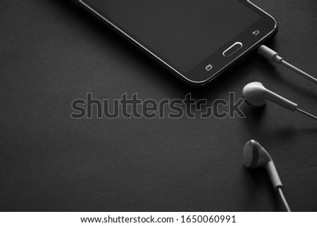 Headphones and smartphone on a dark gray background. Stylish black and white photo.