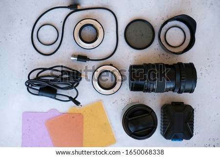 Flat lay composition equipment for professional photographer on grey. Photo gradient filter, macro rings, polarizing filter, charger, video light with color plates, lens caps all for cameras
