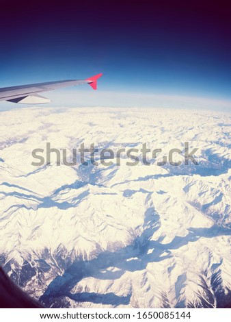 View of an airplane wing over snow capped sharp winter mountains