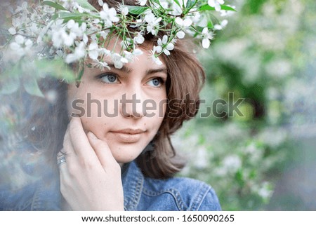 Girl spring. A cute girl of European appearance with a wreath on her head in a denim jacket on a background of flowering trees. Romantic picture. Spring sunny day.