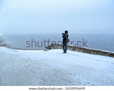 A man with a camera takes a photo during a winter snowstorm. Photographer and heavy snowfall near the Peter and Paul Fortress in St. Petersburg, Russia.