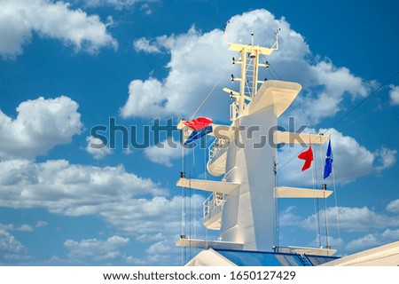 The white communication tower of a cruise ship with colorful flags and banners against a blue sky